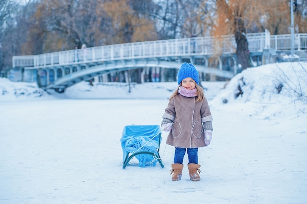 Zdjęcie portret dziewczynki z saniami na tle śniegu w parku