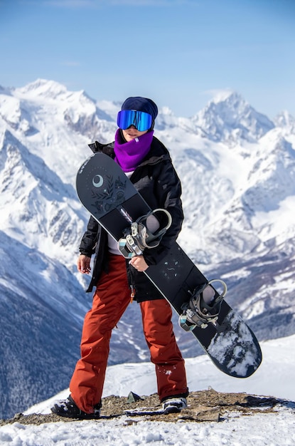 Zdjęcie portret dziewczynki z snowboardem na szczycie zaśnieżonej góry.