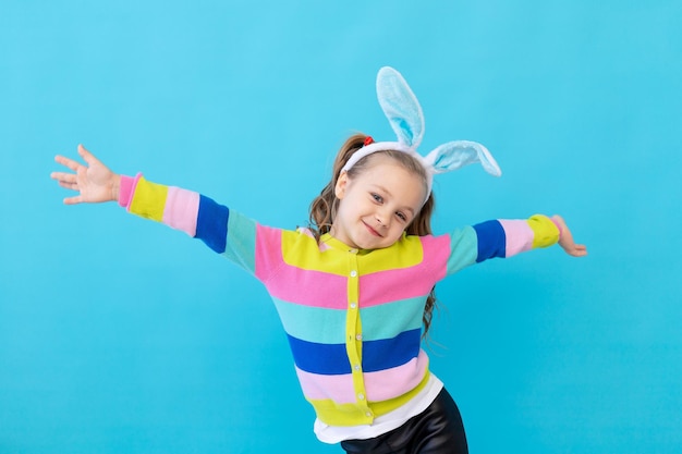 Portret Dziewczynki Z Uszami Królika W Pasiastej Kurtce, Uśmiechając Się I Oddając Pojęcie święta Wielkanocnego Niebieskie Tło Studio Fotograficzne Miejsce Na Tekst