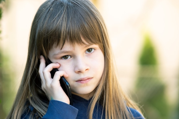 Portret dziewczyny ładne dziecko z długimi włosami rozmawia przez telefon komórkowy. Małe dziecko kobiece komunikacji za pomocą smartfona. Koncepcja komunikacji dzieci.