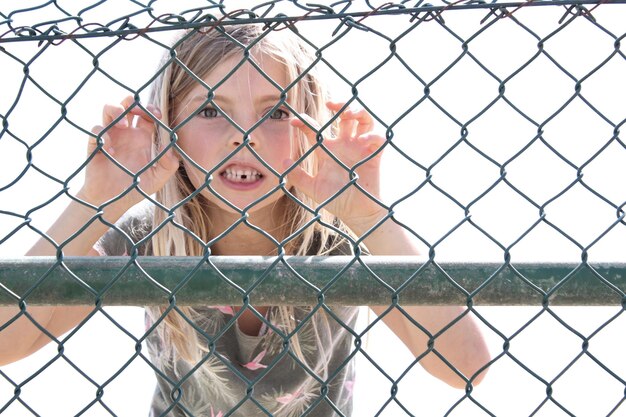 Zdjęcie portret dziewczyny robiącej twarz widziany przez ogrodzenie łańcuchowe
