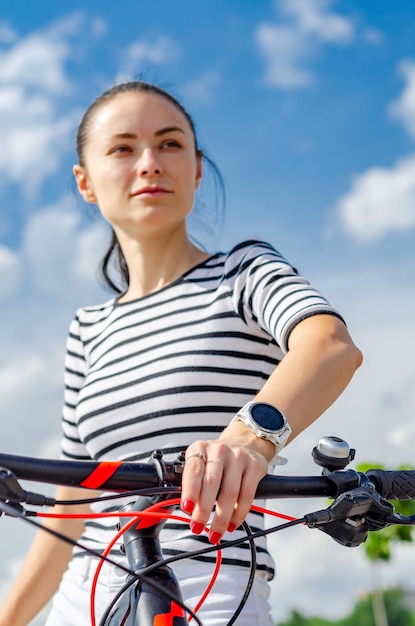 Zdjęcie portret dziewczyny rowerzystki na rękę nieba z inteligentnym zegarkiem na kierownicy roweru