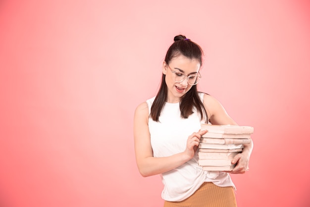 Portret dziewczyny student w okularach na różowej ścianie z książkami w dłoniach. Pojęcie edukacji i hobby.