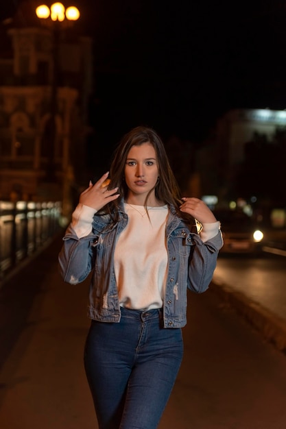 Portret dziewczyny studenta spaceru na ulicy w nocy Stylowa atrakcyjna młoda kobieta w mieście wieczorem denim jacket