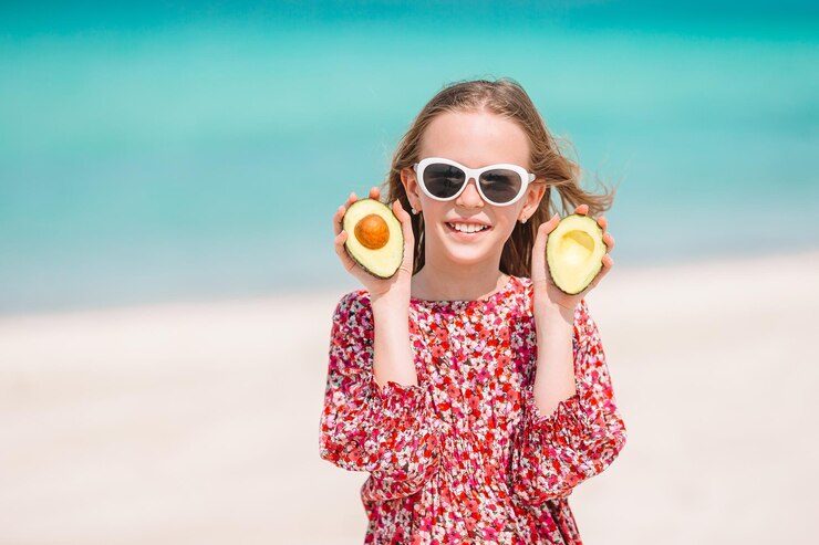 Zdjęcie portret dziewczyny trzymającej awokado na plaży