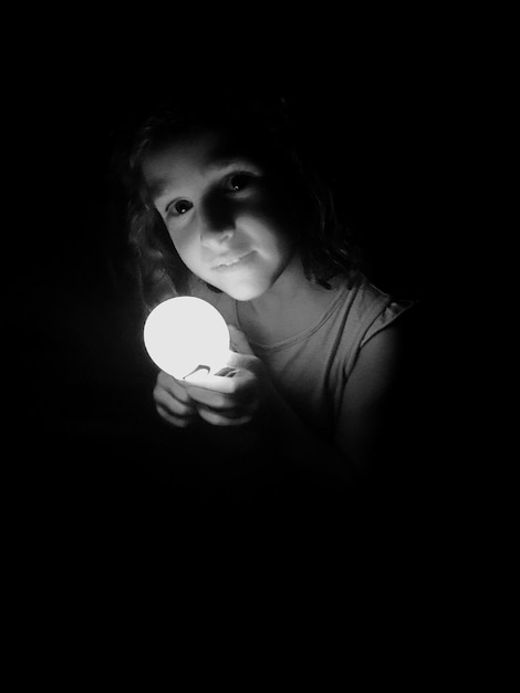 Zdjęcie portret dziewczyny trzymającej oświetloną żarówkę na czarnym tle