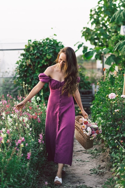 Portret dziewczyny z długimi włosami z koszem kwiatów. Spacer po ogrodzie kwiatowym. Dziewczyna i kwiaty. Florystyka.