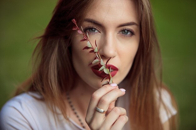 Portret dziewczyny z jasnym makijażem i ustami Marsala z czerwoną rośliną