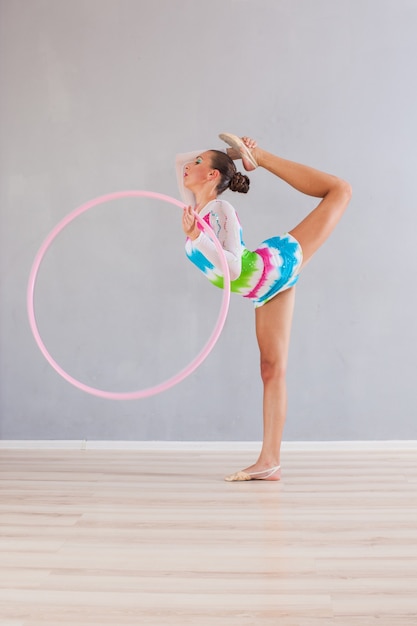 Portret elastycznej gimnastyczki, która robi akrobatyczny wyczyn z różowym obręczem
