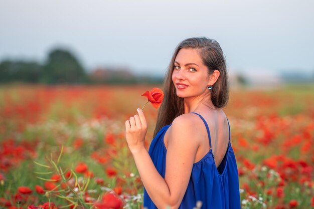 Portret eleganckiej młodej kobiety z długimi włosami w polu maku w wieczornym słońcu