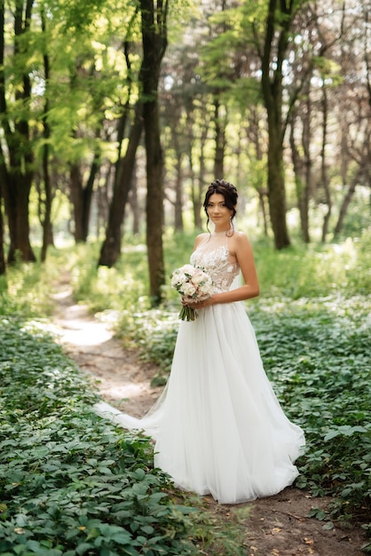 Portret eleganckiej panny młodej dziewczyny na ścieżce w lesie liściastym z bukietem