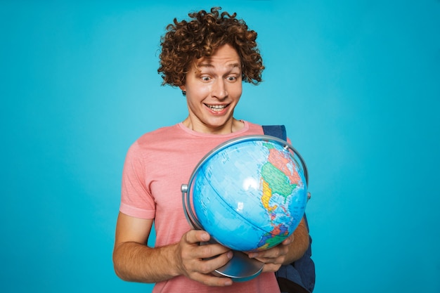Portret europejski studencki facet jest ubranym plecaka uśmiecha się ziemską kulę ziemską z kędzierzawym włosy i trzyma
