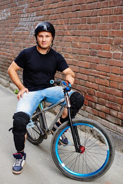 Portret faceta w kasku na rowerze siedzącym pod ścianą z czerwonej cegły