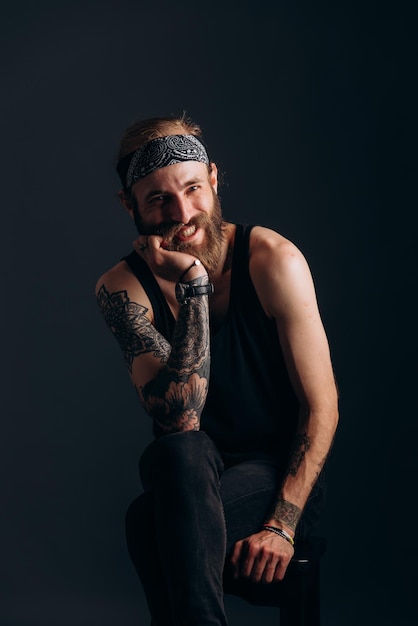 Portret faceta z brodą i tatuażami na ciemnym tle hipster