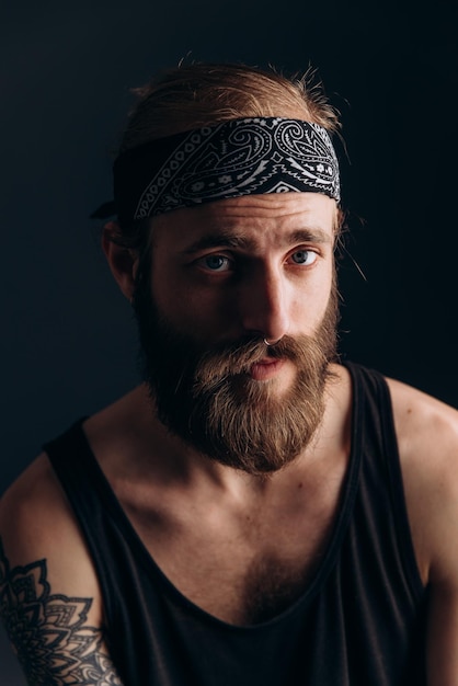 Portret faceta z brodą i tatuażami na ciemnym tle hipster