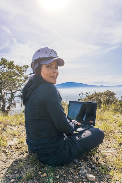 Portret freelancerki z laptopem siedzącej na skale na szczycie góry