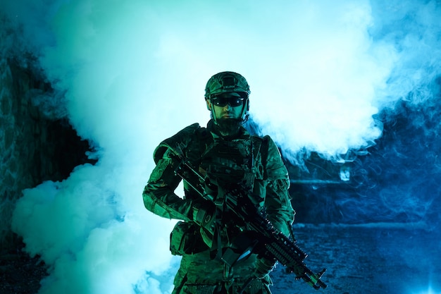 Portret gracza airsoft w profesjonalnym sprzęcie z karabinem maszynowym w opuszczonym zrujnowanym budynku. Żołnierz z bronią na wojnie w dymie i mgle
