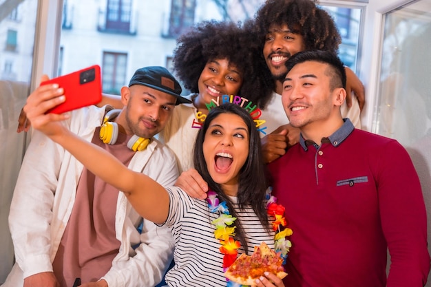 Portret grupy przyjaciół jedzących pizzę na tarasie w domu w dniu urodzin, biorących pamiątkowe selfie