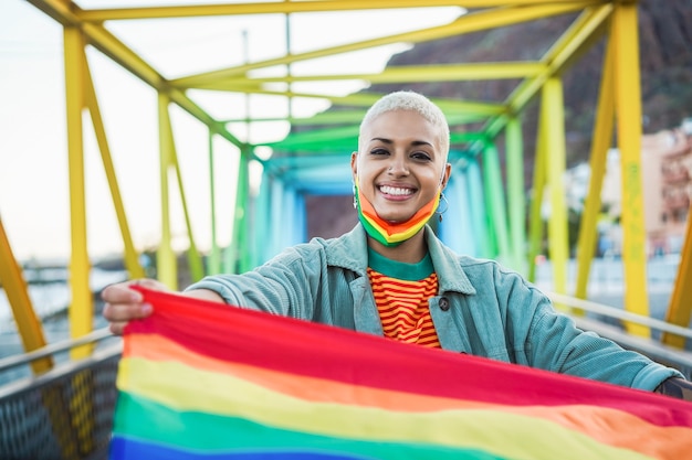 Portret homoseksualnej kobiety z maską trzyma tęczową flagę - koncepcja praw LGBT - skupić się na twarzy dziewczyny