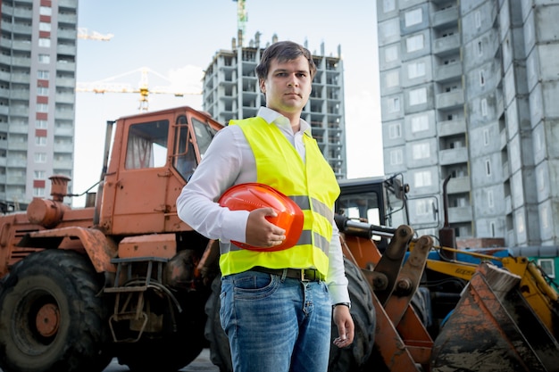 Portret inspektora budowlanego pozującego obok koparki na placu budowy