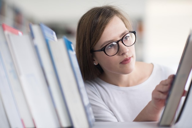 Zdjęcie portret inteligentnie wyglądającej słabej studentki w szkolnej bibliotece wybierającej książkę do przeczytania z półki