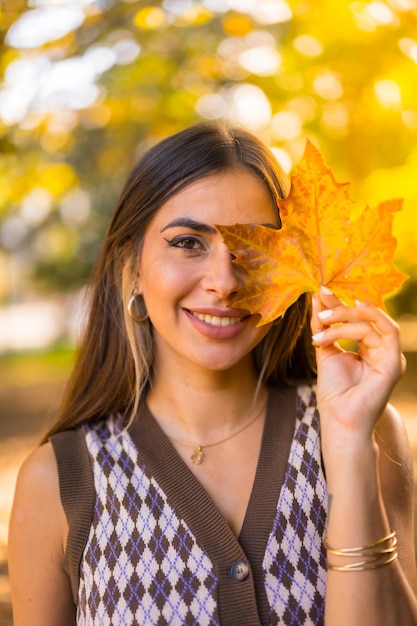 Portret kaukaskiej brunetki jesienią w naturalnym parku z liściem na twarzy o zachodzie słońca