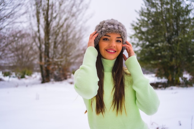 Portret kaukaskiej brunetki w zielonym stroju i wełnianym kapeluszu cieszący się śniegiem