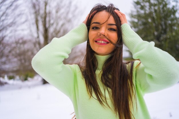 Portret kaukaskiej brunetki w zielonym stroju i wełnianym kapeluszu cieszący się śniegiem