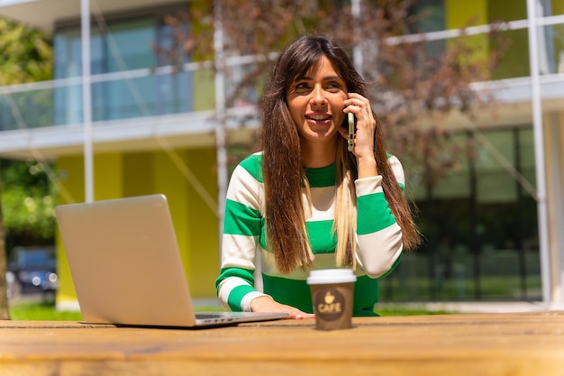 Portret kaukaskiej dziewczyny pracującej z komputerem w naturze rozmawiającej przez telefon