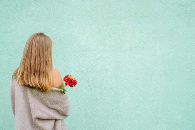 Portret Kobiety Blondynka Z Kwiatem Stojący Przed Niebieską ścianą. Widok Z Tyłu