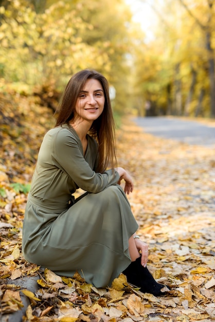 Portret kobiety brunetka w zielonej sukni pozowanie w parku jesienią