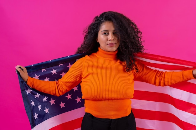 Portret kobiety curlyhaired uśmiechając się z flagą usa na różowym tle studio strzał