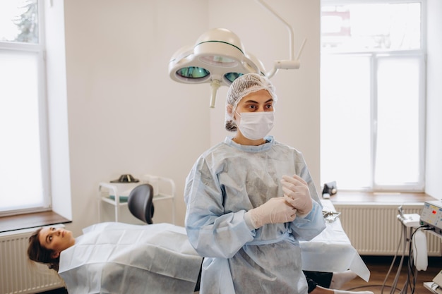 Portret kobiety-lekarki, chirurga w niebieskich zaroślach, zakładających rękawiczki chirurgiczne i patrzących na kamerę