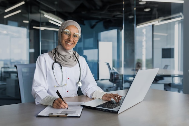 Portret kobiety lekarz w hidżab muzułmanin pracujący w nowoczesnym biurze wewnątrz kliniki uśmiecha się i patrzy