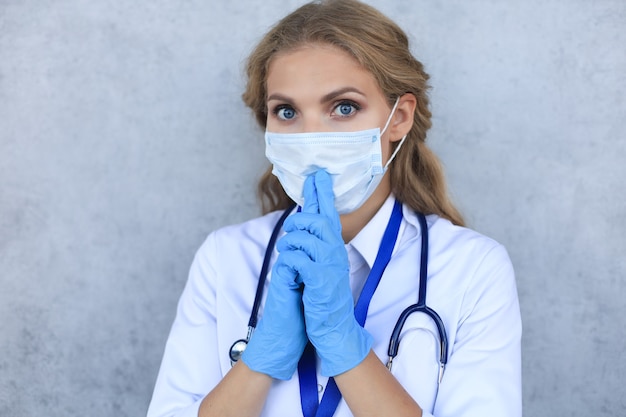 Portret kobiety lekarz ze stetoskopem w masce na białym tle nad szarym tłem.
