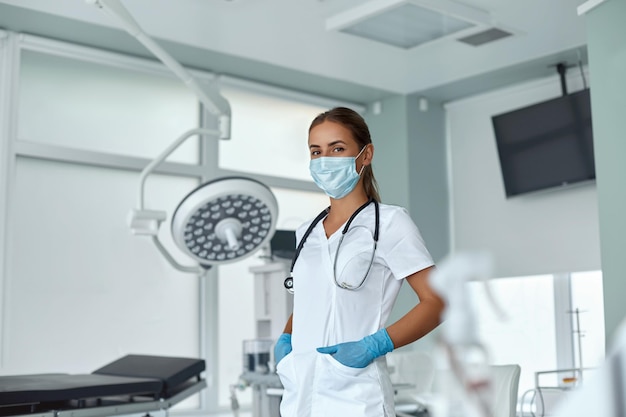 Portret kobiety młody lekarz w masce medycznej i stetoskopie białego fartucha na szyi w klinice