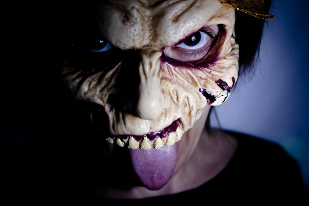Portret kobiety noszącej maskę, wystawiającej język w ciemni