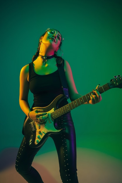 Portret kobiety rasy kaukaskiej gitarzysty na białym tle na zielonym tle studia w świetle neonowym