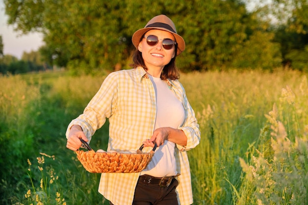 Portret kobiety rolnik w kapeluszu z koszem świeżego jajka. Rolnictwo, uprawa ekologicznych produktów ekologicznych. Wiejska droga, wieś, zachód słońca, przyroda, tło ogrodu