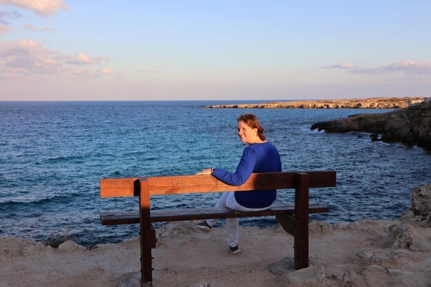 Zdjęcie portret kobiety siedzącej na ławce patrzącej na brzeg morza na tle nieba