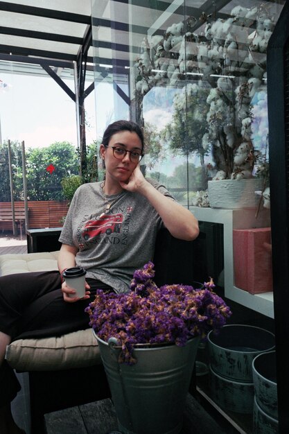 Zdjęcie portret kobiety siedzącej przy fioletowych roślinach kwitnących przy oknie