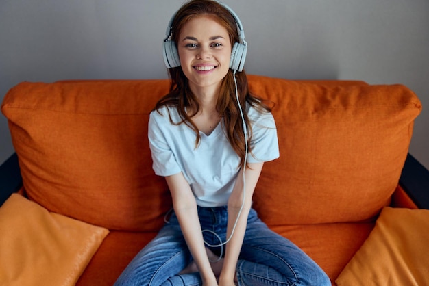 Portret kobiety słuchającej muzyki przez słuchawki na pomarańczowej kanapie bez zmian Zdjęcie wysokiej jakości