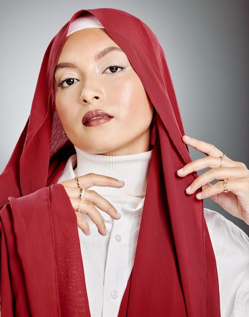 Portret kobiety ubranej w czerwony hidżab na szarym tle studia i copyspace Młoda muzułmanka w chuście pozuje i pokazuje promienną skórę makijaż rzęs i biżuterię