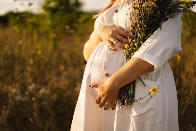 Portret kobiety w ciąży piękna młoda kobieta w ciąży w białej sukni spaceruje po polu
