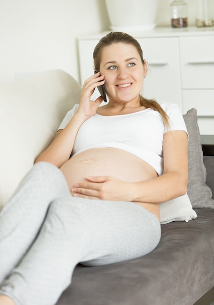 Portret kobiety w ciąży siedzącej na kanapie i rozmawiającej przez telefon