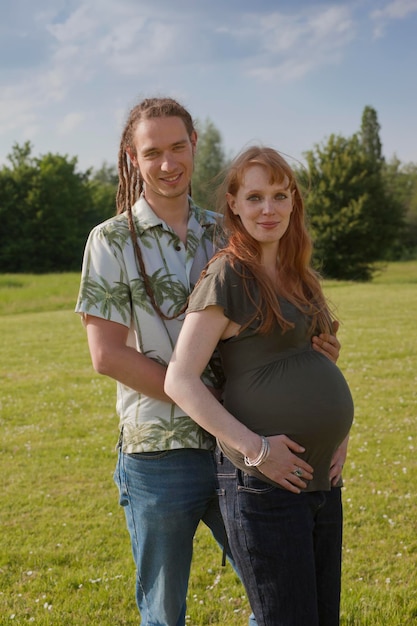 Zdjęcie portret kobiety w ciąży stojącej z chłopakiem na trawiastym polu