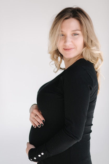 Portret kobiety w ciąży w studio na białym tle piękna przyszła matka położyła jej ręce
