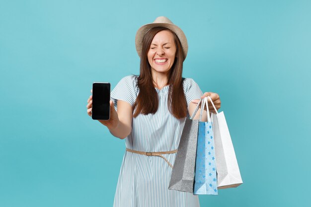 Portret Kobiety W Letniej Sukience, Słomkowy Kapelusz, Trzymając Pakiety Torby Z Zakupami Po Zakupach, Telefon Komórkowy Z Pustym Ekranem Na Białym Tle Na Niebieskim Tle Pastelowych. Skopiuj Miejsce Na Reklamę.