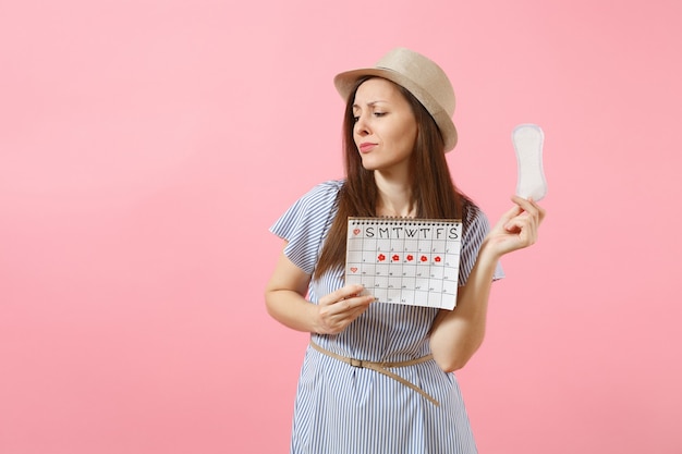 Zdjęcie portret kobiety w niebieskiej sukience, kapeluszu trzymając podpaskę, kalendarz kobiet okresów do sprawdzania dni menstruacji na białym tle na różowym tle. medycyna, opieka zdrowotna, koncepcja ginekologiczna. skopiuj miejsce