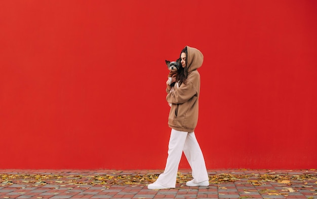 portret kobiety w stylowych, codziennych ubraniach idących ulicą na tle czerwonej ściany